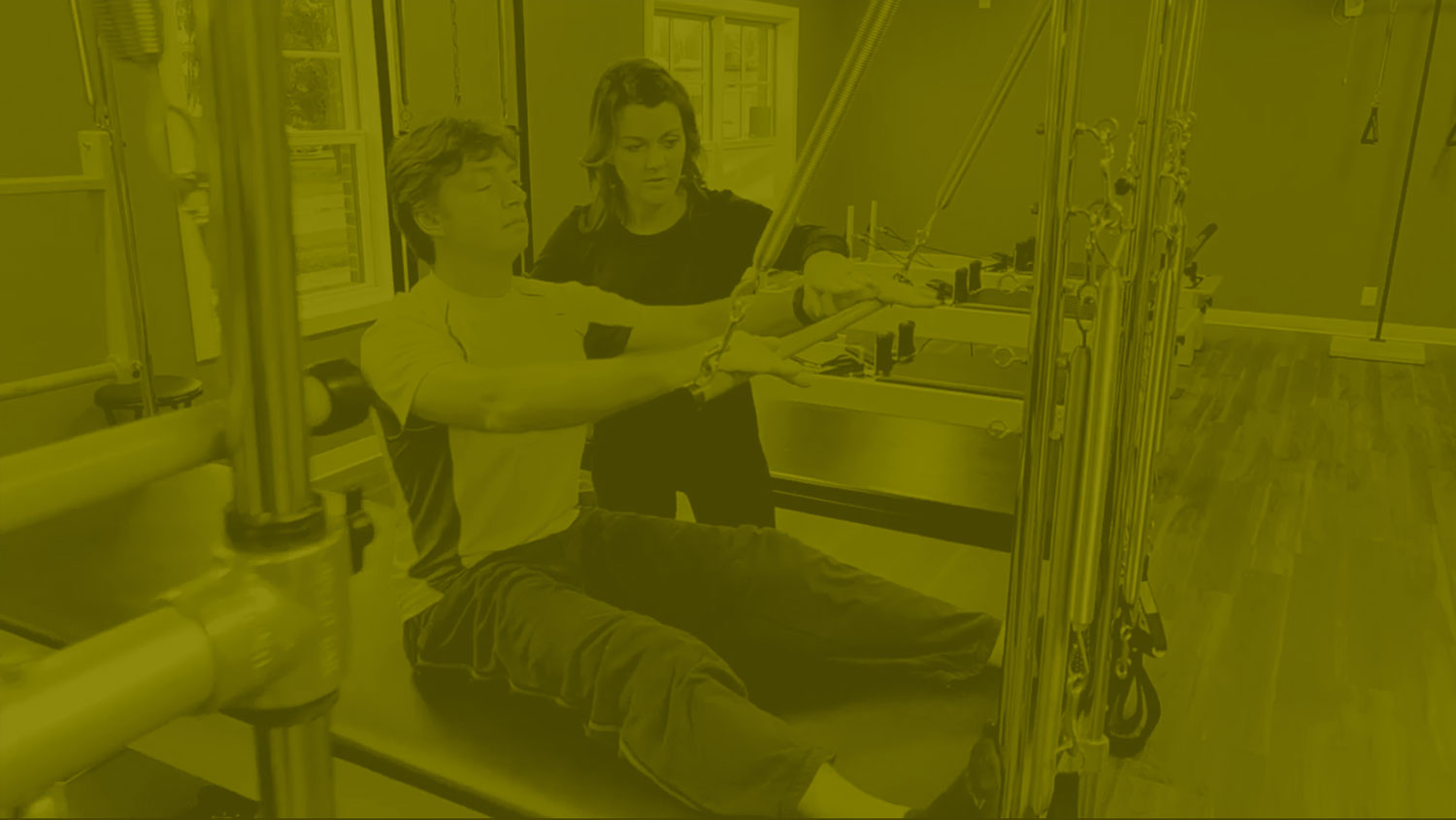 Instructor with student on Cadillac Reformer - low contrast chartreuse color tinted background